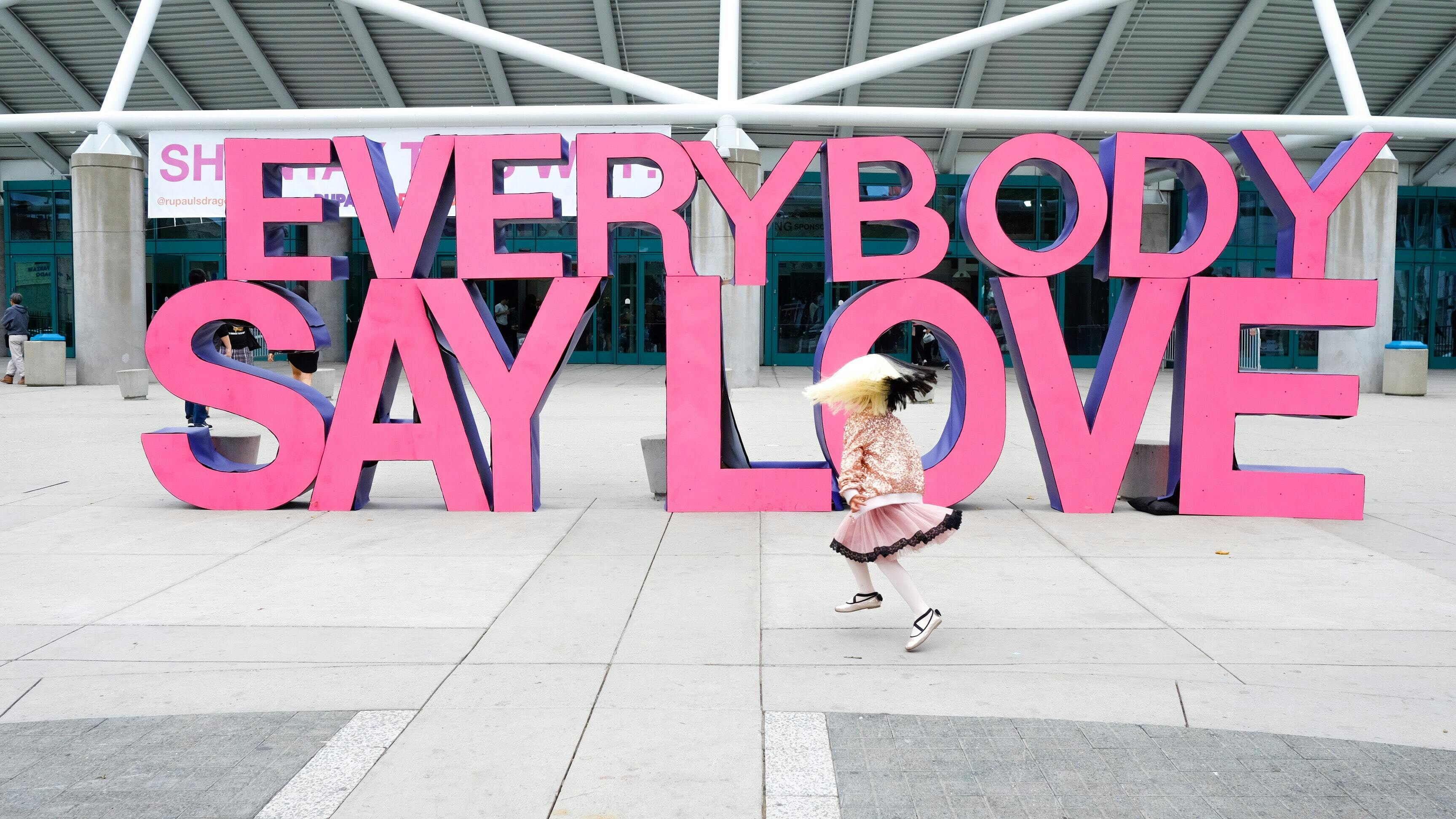 Een grote set roze hoofdletters met het opschrift Everybody say love op een groot plein voor de ingang van een etablissement.