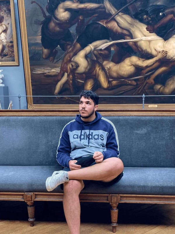 Young white man in a museum sitting on a couch in front of a painting