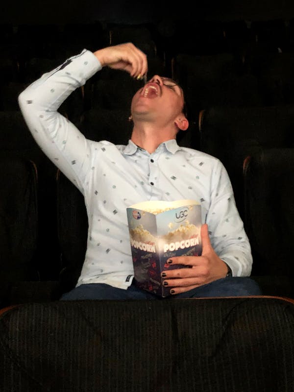 Jonge blanke man met bril eet popcorn in een bioscoop