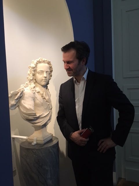 Well-dressed white man in front of a painting of Peter I the Great